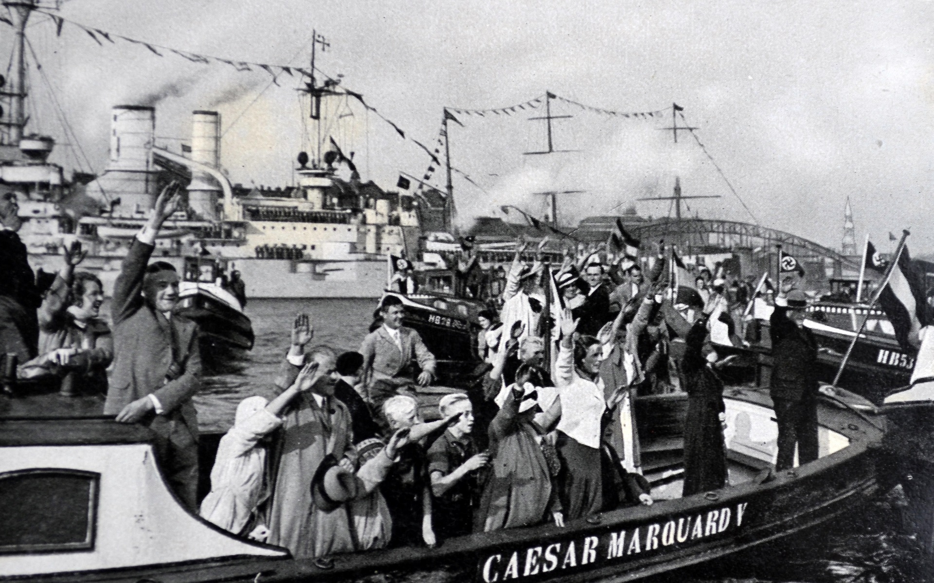 Zu sehen sind jubelnde Menschen auf einem Boot, welches die Aufschrift "Caesar Marquard V" trägt. Im Hintergrund fahren weitere Schiffe, die Umrisse des Hamburger Hafens sind zu sehen.